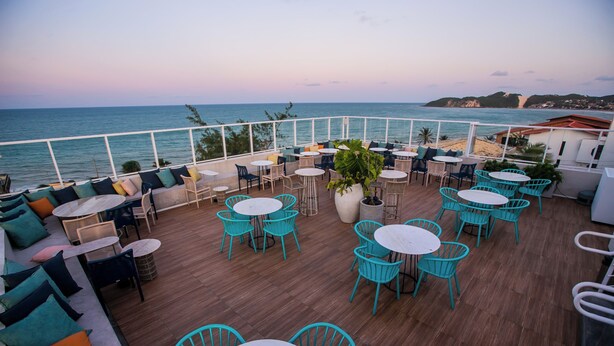 Una terraza con mesas y sillas redondas, una planta en maceta y vistas al mar.