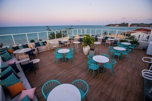 Una terraza con mesas y sillas redondas, una planta en maceta y vistas al mar.