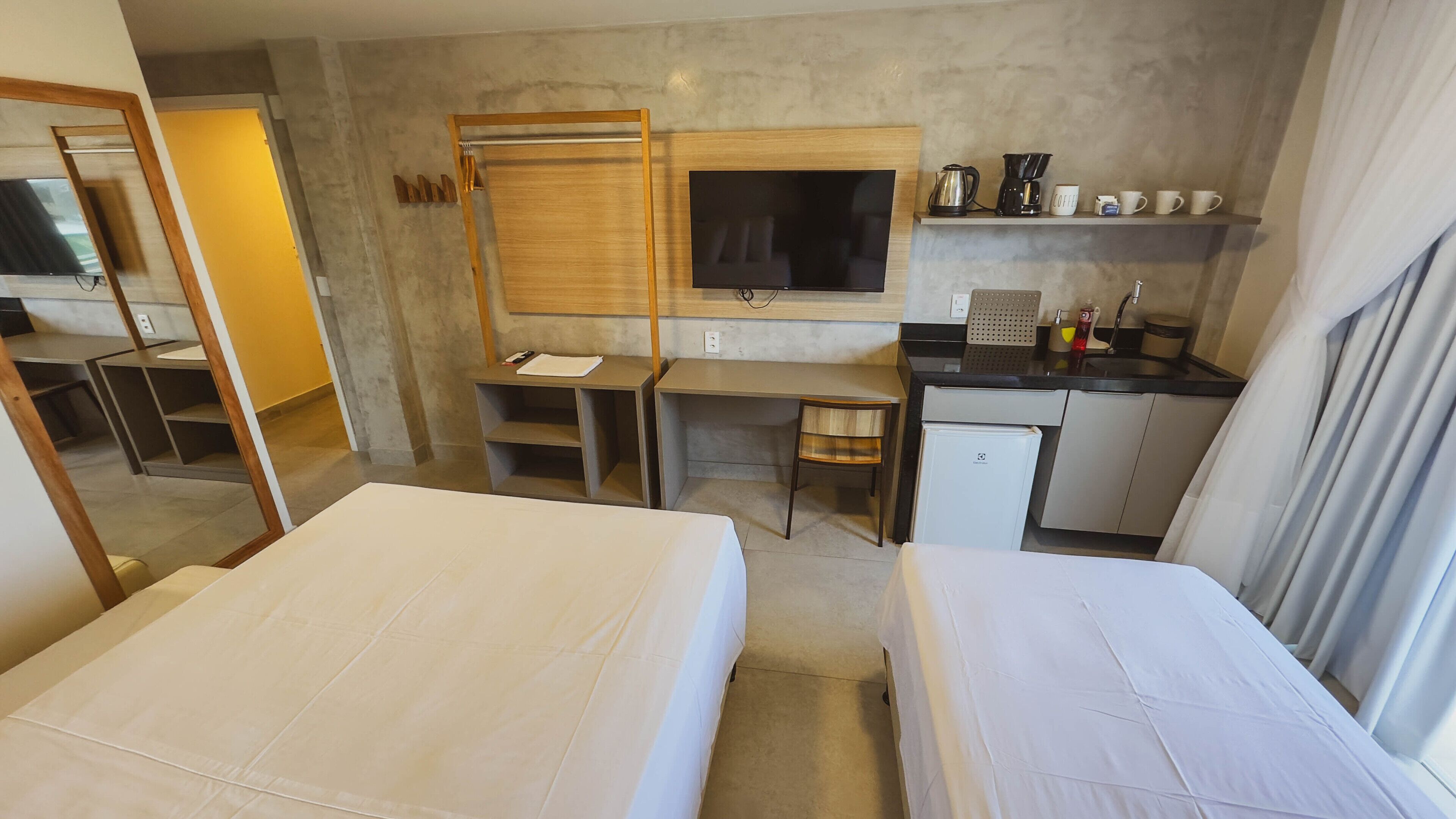 A hotel room with two beds, a desk, a television, a coffee maker, and a small refrigerator.