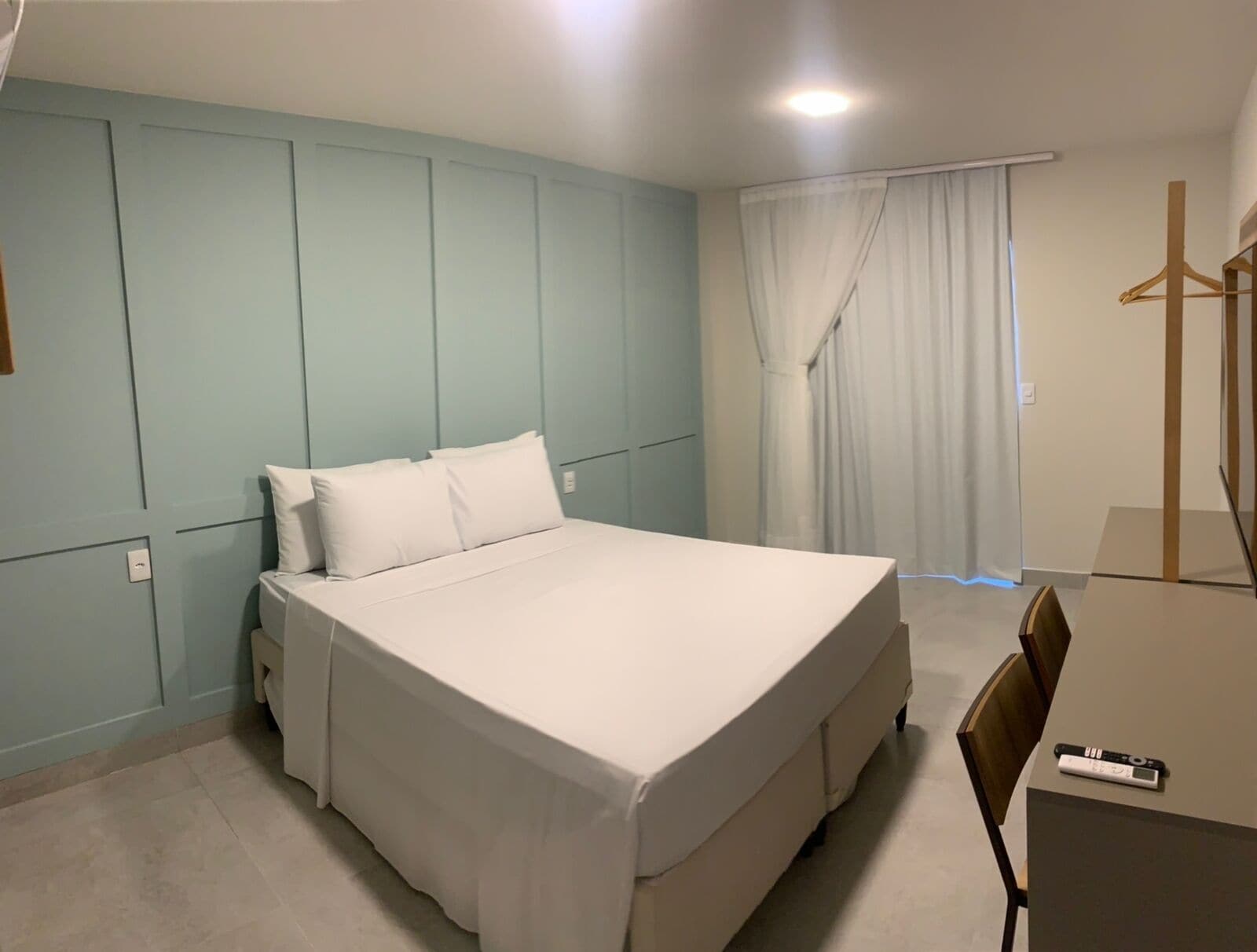A bedroom with a bed, a chair, a desk, and a hanging coat rack.