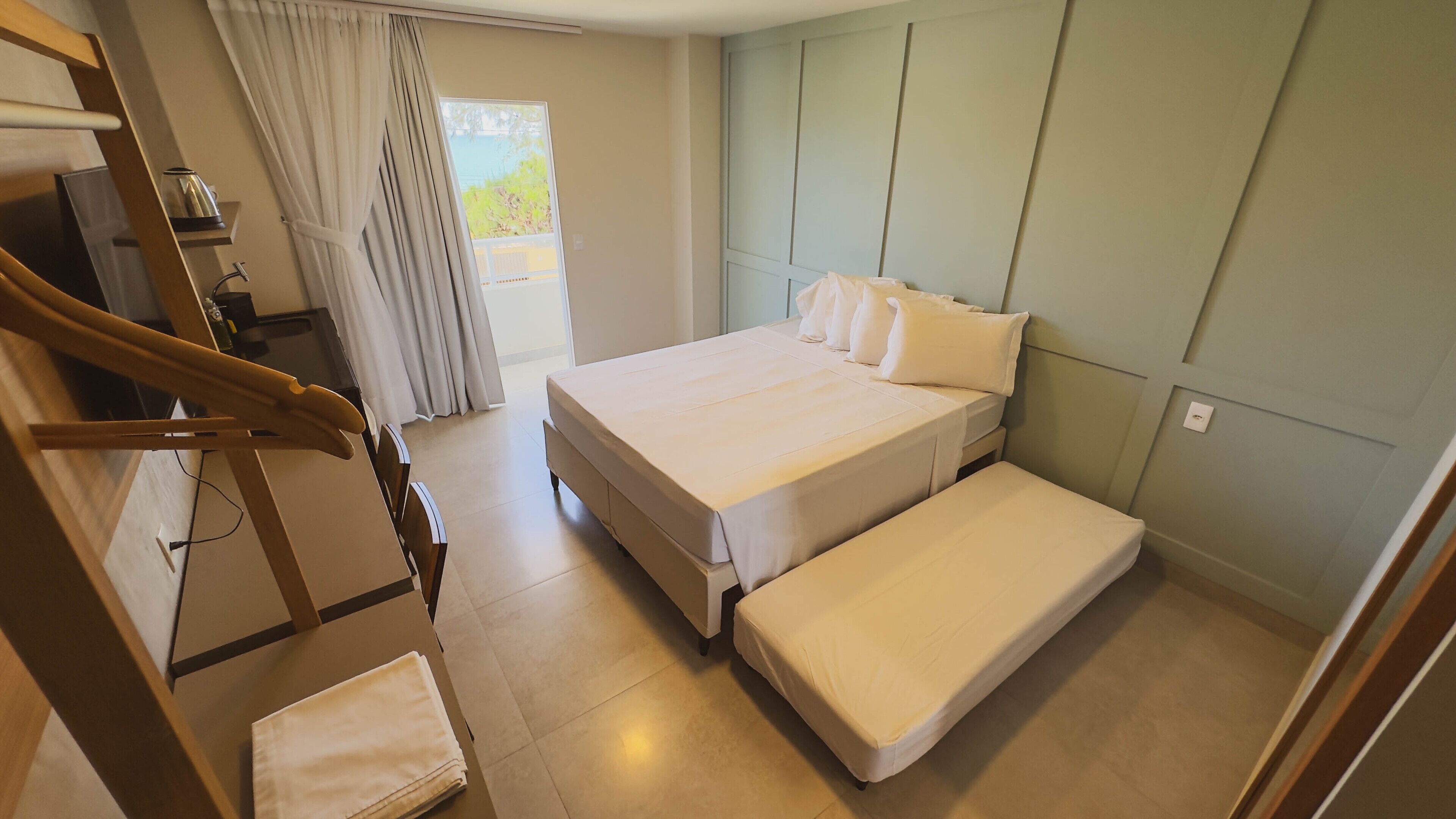 A bedroom with a bed, a bench, a wooden chair, a small table, and a window with curtains.