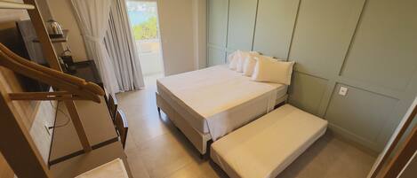 A bedroom with a bed, a bench, a wooden chair, a small table, and a window with curtains.