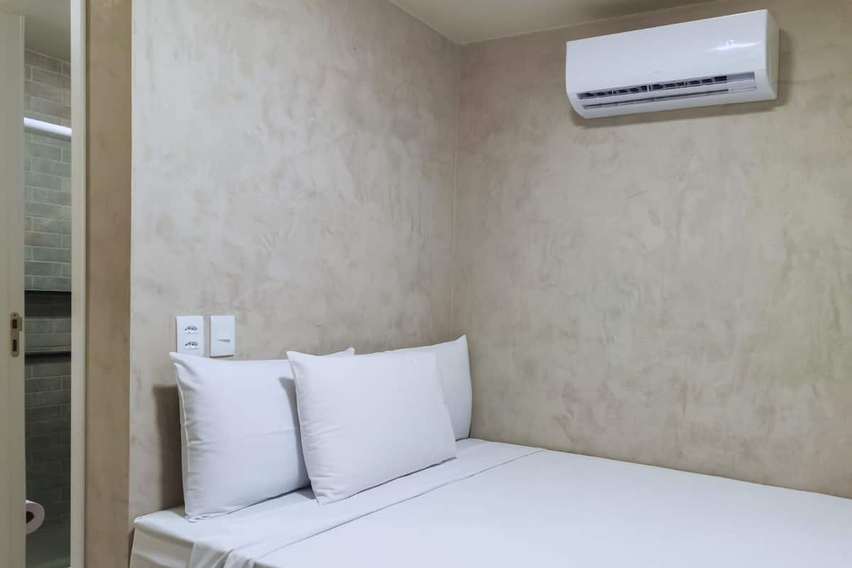 A hotel room with a bed, white pillows, a wall-mounted air conditioner, and a door leading to a bathroom with a toilet.