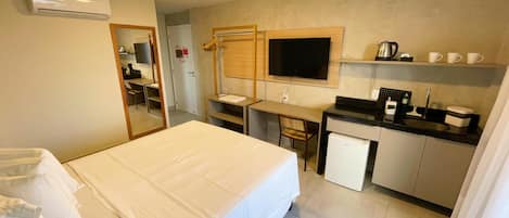 Habitación de hotel compacta con cama, escritorio, kitchenette pequeña y televisión.