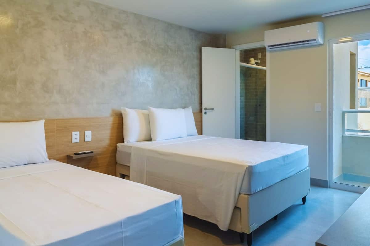 A hotel room with two beds, a wardrobe, an air conditioning unit, and a balcony with a view.