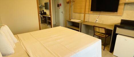 Quarto de hotel com cama, escrivaninha, televisão e mini-geladeira.
