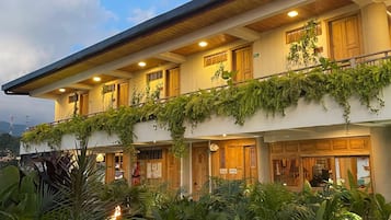 Un edificio de varios pisos con techo plano, balcones de madera y abundante vegetación.