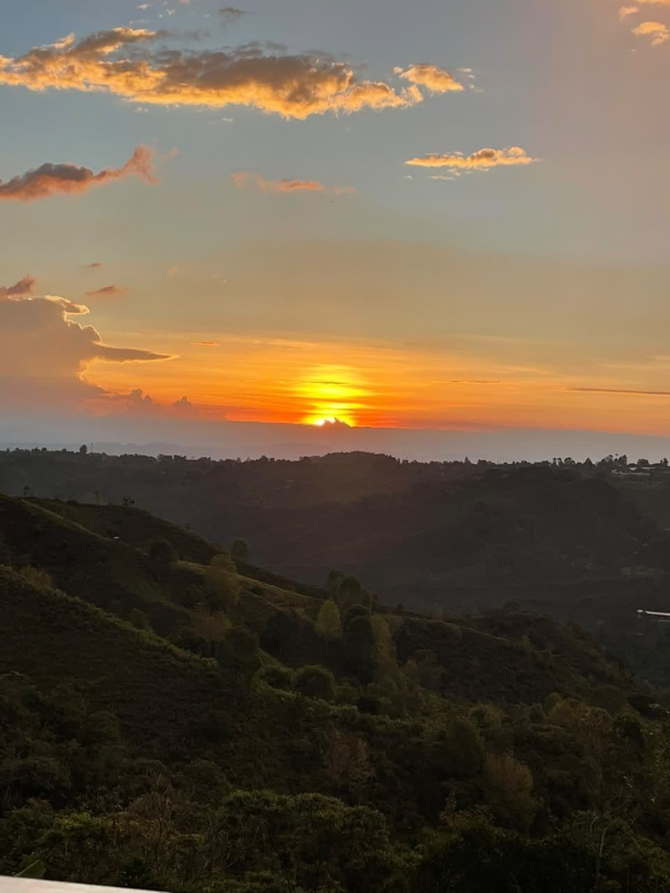 A sunset over a hilly landscape with a view of the horizon.