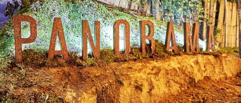 A sign with the word "PANORAMA" in large letters, set against a backdrop of a dirt embankment and wooden fence.