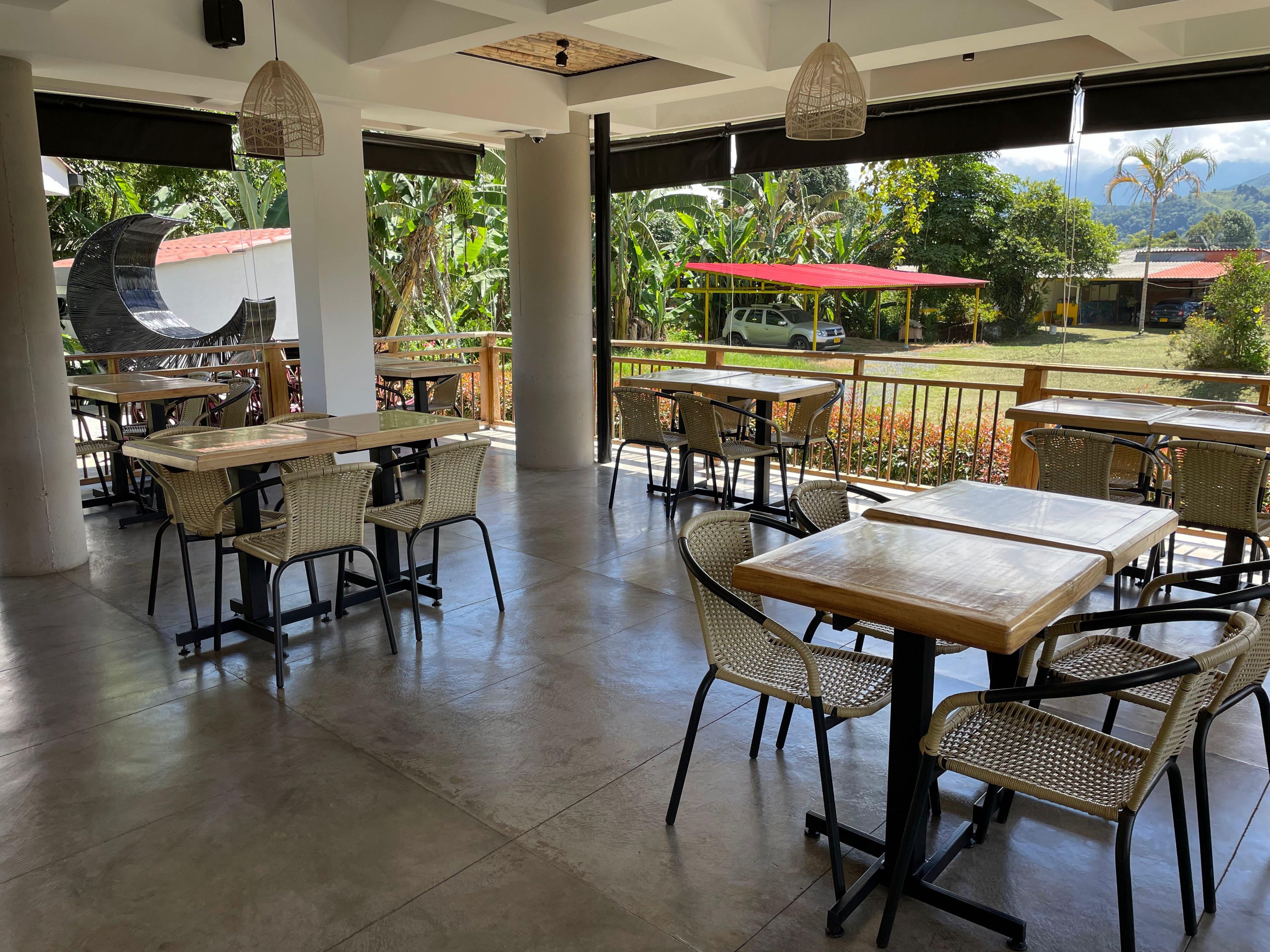 An outdoor dining area with tables and chairs, a grill, and a view of a lush garden and distant buildings.