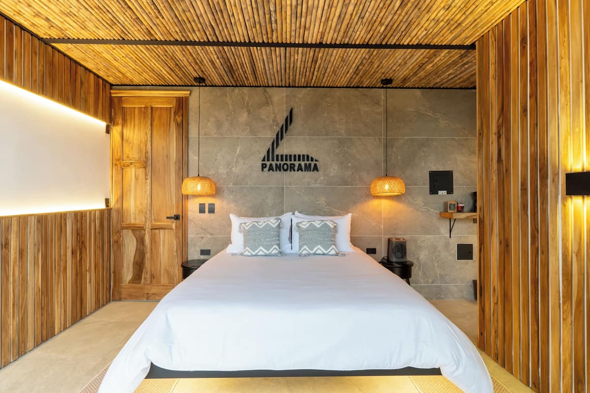 A large bed with white bedding, two wall-mounted lamps, and a wooden ceiling.