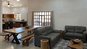Ein modernes Wohnzimmer mit grauem Sofa, einem Holztisch und einer Essecke mit einer hölzernen Bank.