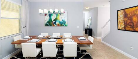 A modern dining area with a wooden table, white chairs, and a colorful abstract painting above.