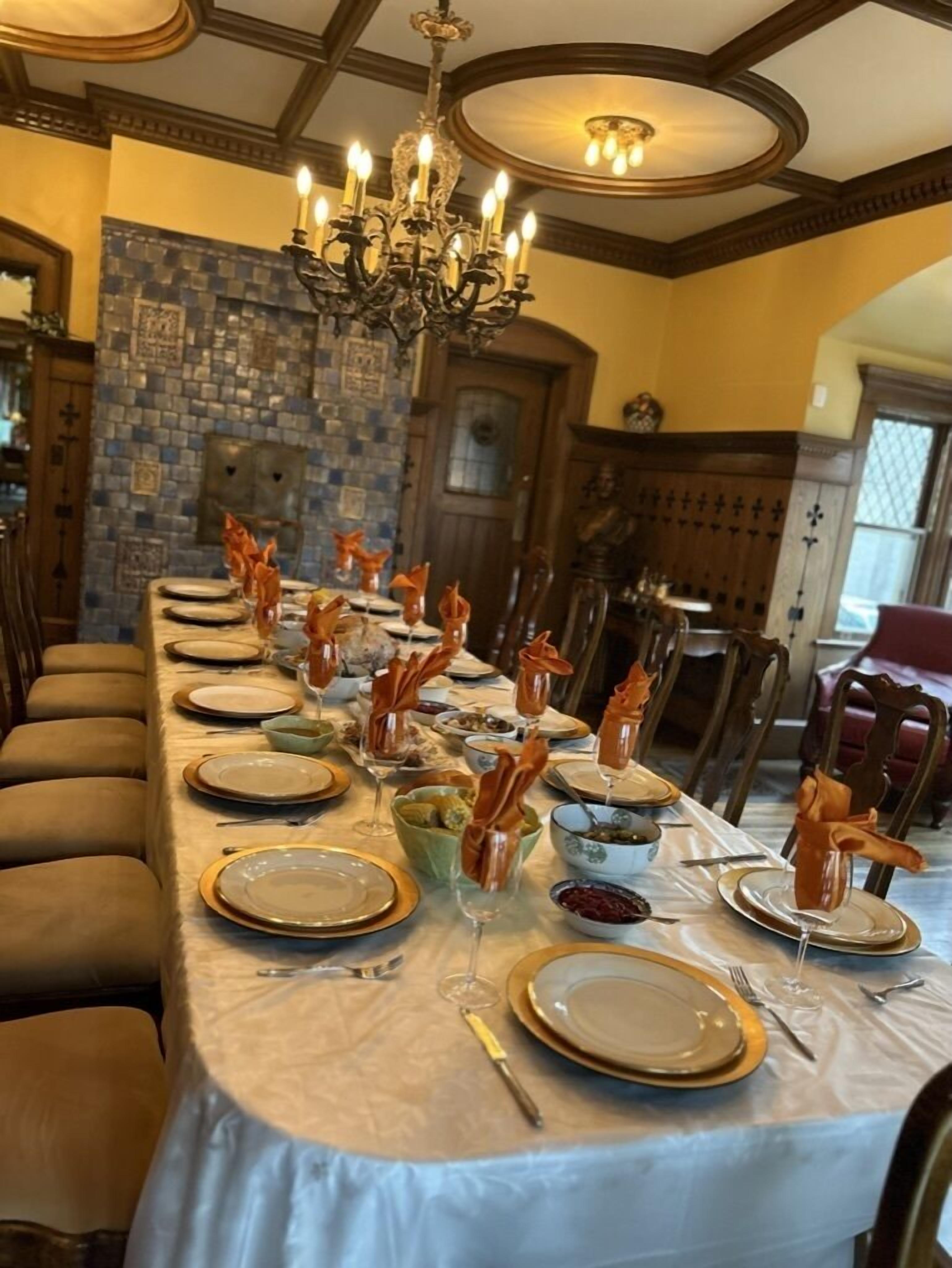 A long dining table set with plates, glasses, and napkins, surrounded by wooden chairs.