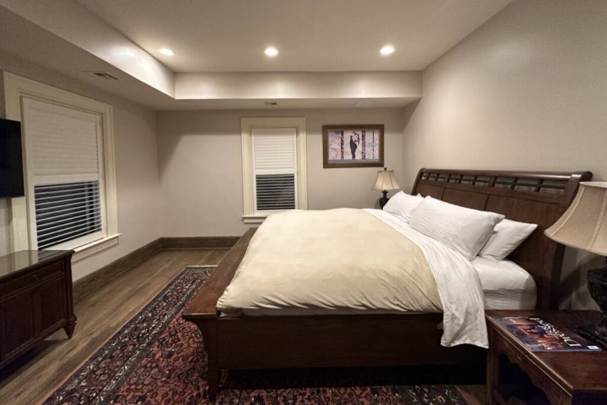 Ein Schlafzimmer mit einem großen Bett, einem Holzkopfstück, einem Nachttisch, einer Lampe und einem Fernseher auf einem Schrank.