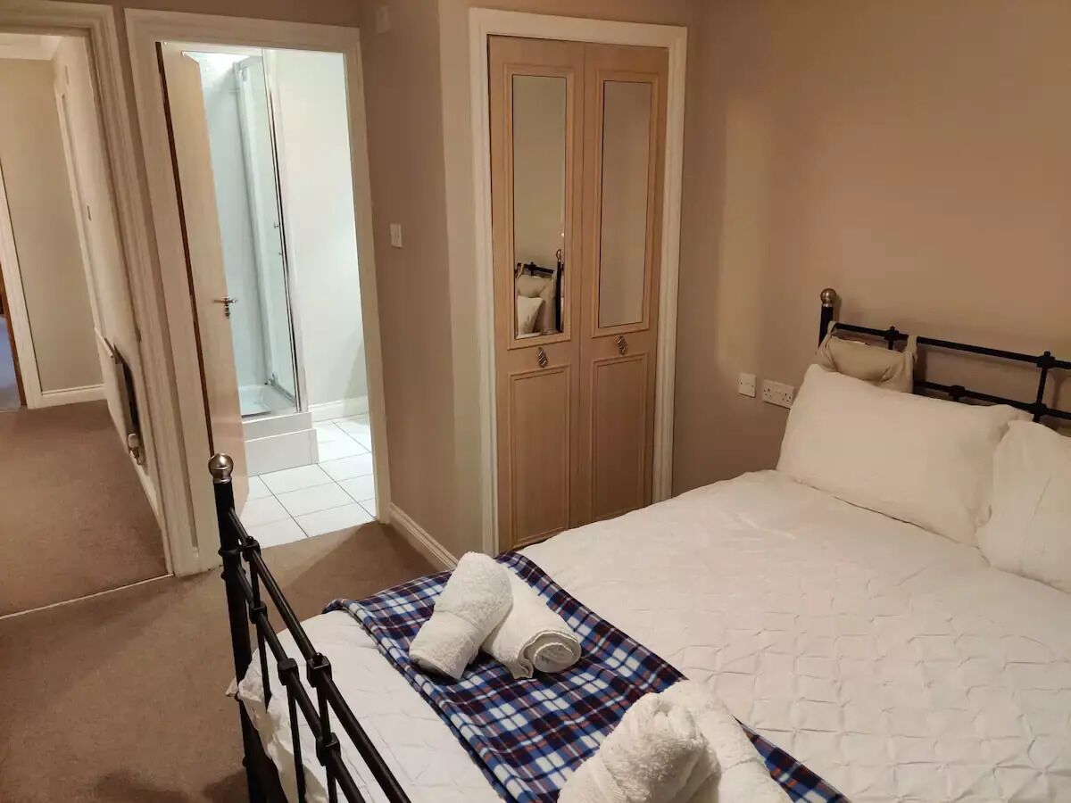 Une chambre à coucher avec un lit, une armoire en bois et une salle de bain visible à travers une porte ouverte.