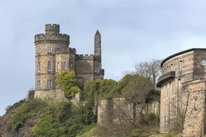 Um castelo de pedra histórico com uma torre redonda e um obelisco alto.