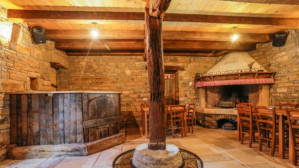 A rustic stone-walled room with a stone fireplace, wooden furniture, and a large wooden post. - Apartment Baladur (Koper)