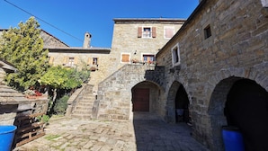 A stone courtyard with a staircase leading to a building with wooden shutters and flower boxes. - Apartment Baladur (Koper)