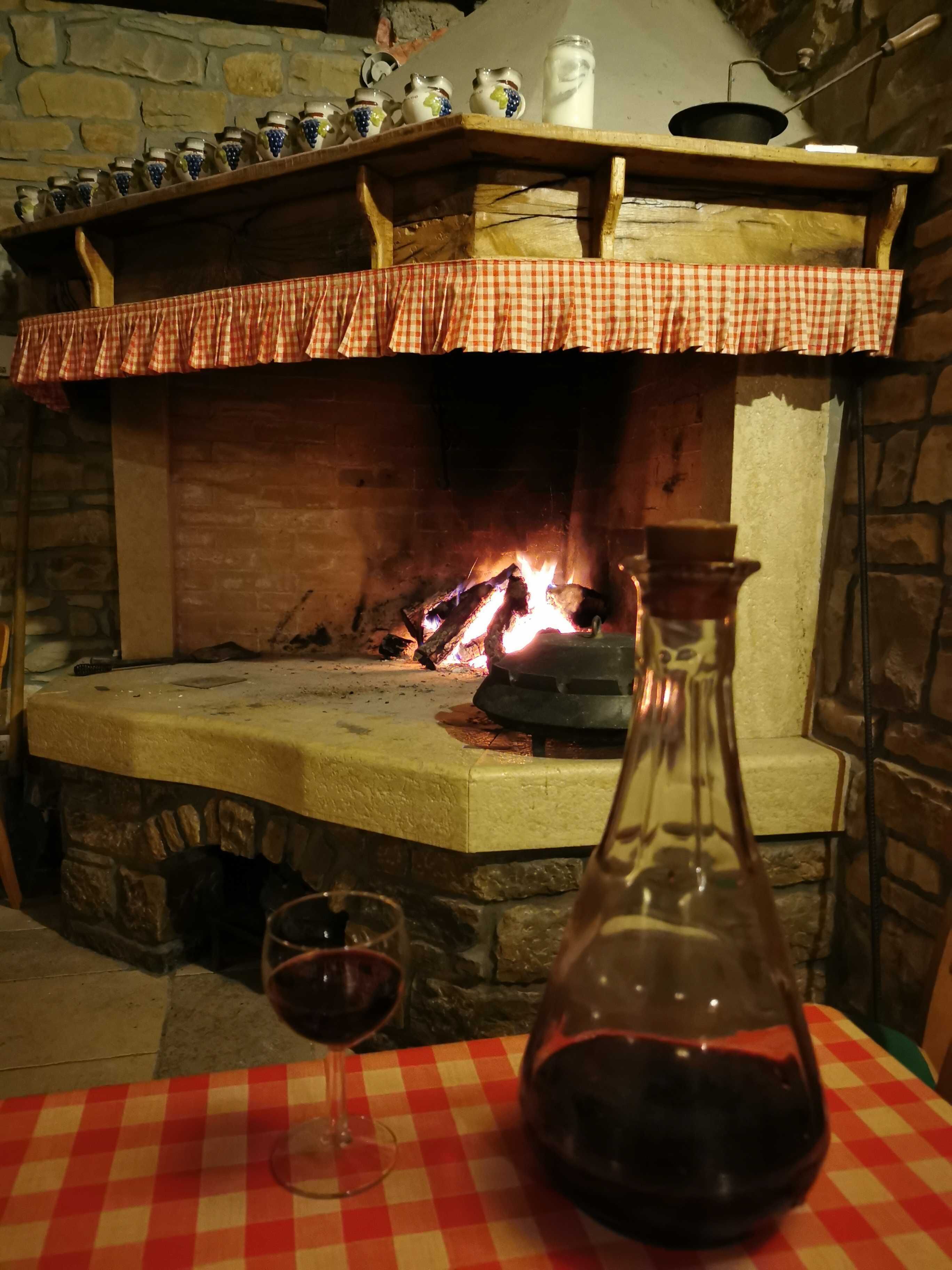 A stone fireplace with a fire, a checkered tablecloth, a wine bottle, and glasses.