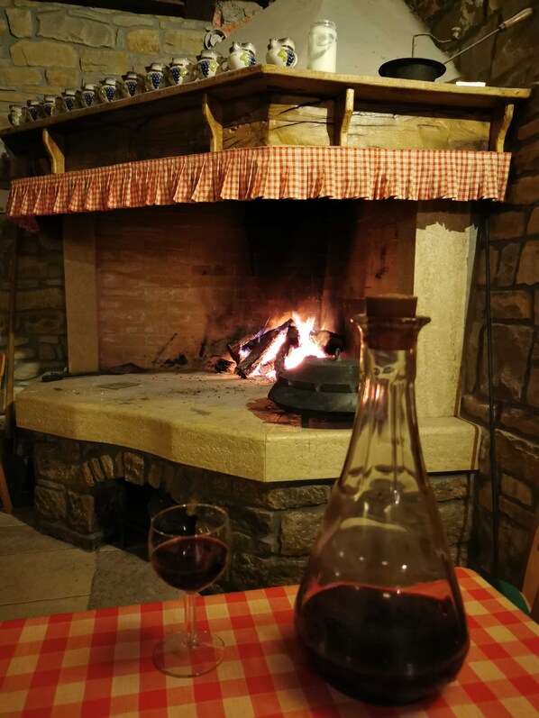 Una chimenea de piedra con fuego, mantel a cuadros, una botella de vino y copas.