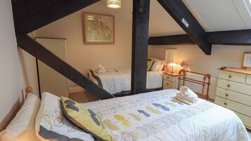 A bedroom with a large bed, a nightstand, a dresser, and a radiator. There is a painting on the wall and a window with a view of the outside.