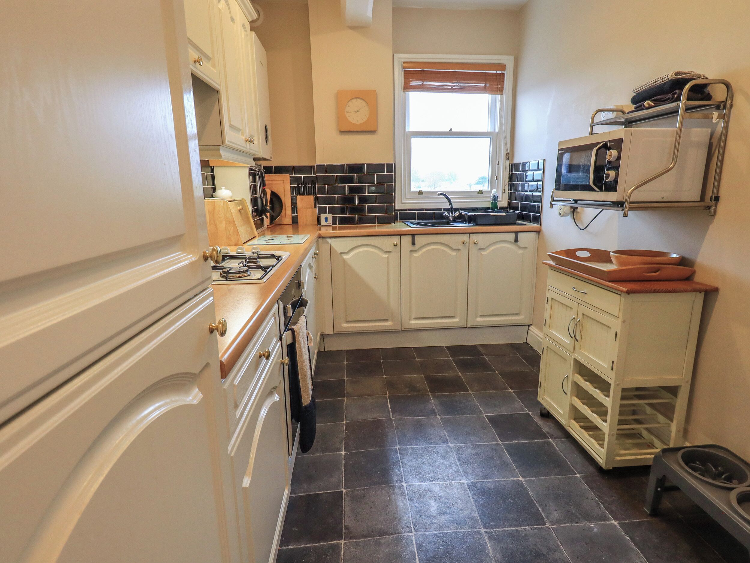 A compact kitchen with white cabinets, a black tiled floor, a stove, a microwave, and a small sink.