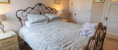 A neatly made bed with a patterned bedspread, a bedside lamp, and a nightstand with drawers.