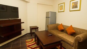 A living room with a sofa, a coffee table, a TV, a refrigerator, and a patterned rug. - Porto Sharm Hotel Apartments (Sharm El Sheikh)