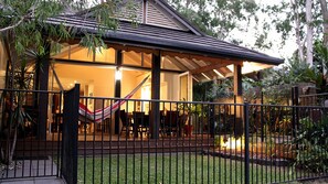 A covered outdoor seating area with a hammock, surrounded by a metal fence and lush greenery.