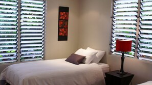 Una habitación de hotel con cama, mesita de noche, lámpara roja y ventana con persianas.