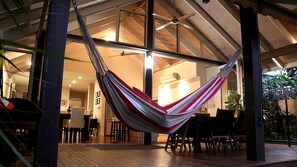 A hammock in a covered outdoor area with wooden flooring and chairs.
