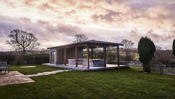 Un pavillon extérieur moderne doté d’une porte en verre, entouré d’une pelouse bien entretenue et d’un chemin en pierre.