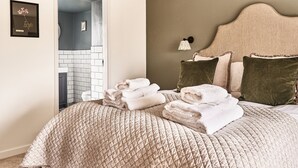 Un lit bien fait, avec des serviettes pliées, une tête de lit agrémentée d’oreillers et un luminaire fixé au mur.