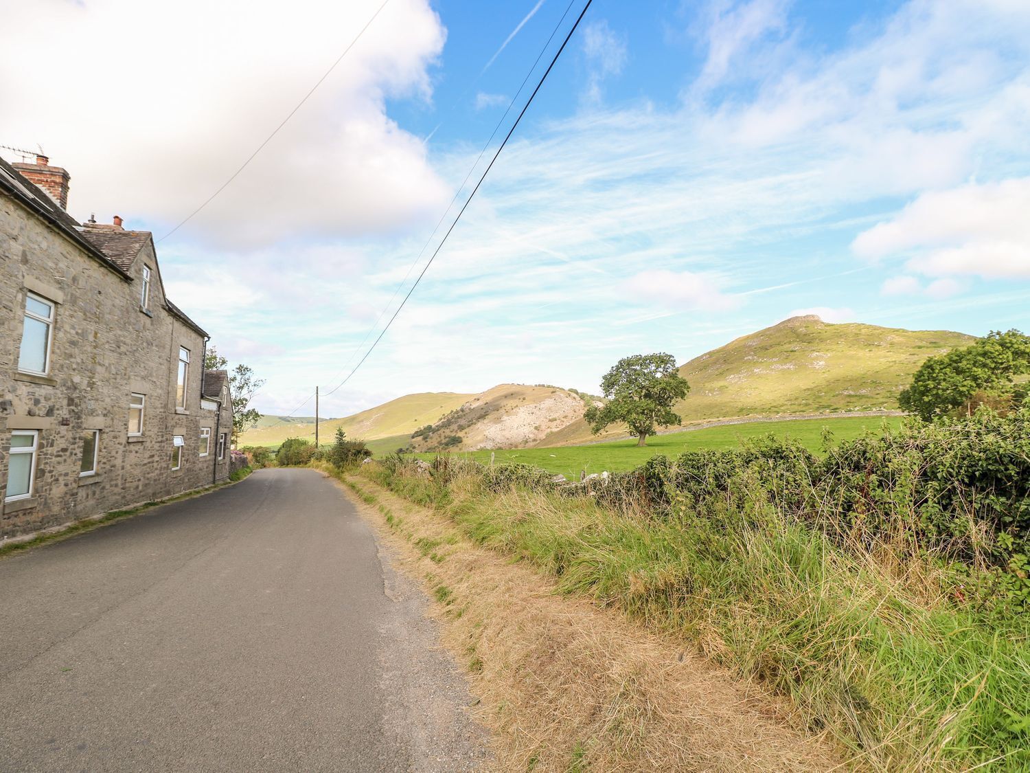 A rural road flanked by stone buildings and green fields.