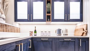 Une cuisine moderne avec des meubles de couleur sombre, un plan de travail blanc et une fenêtre au-dessus de l’évier.