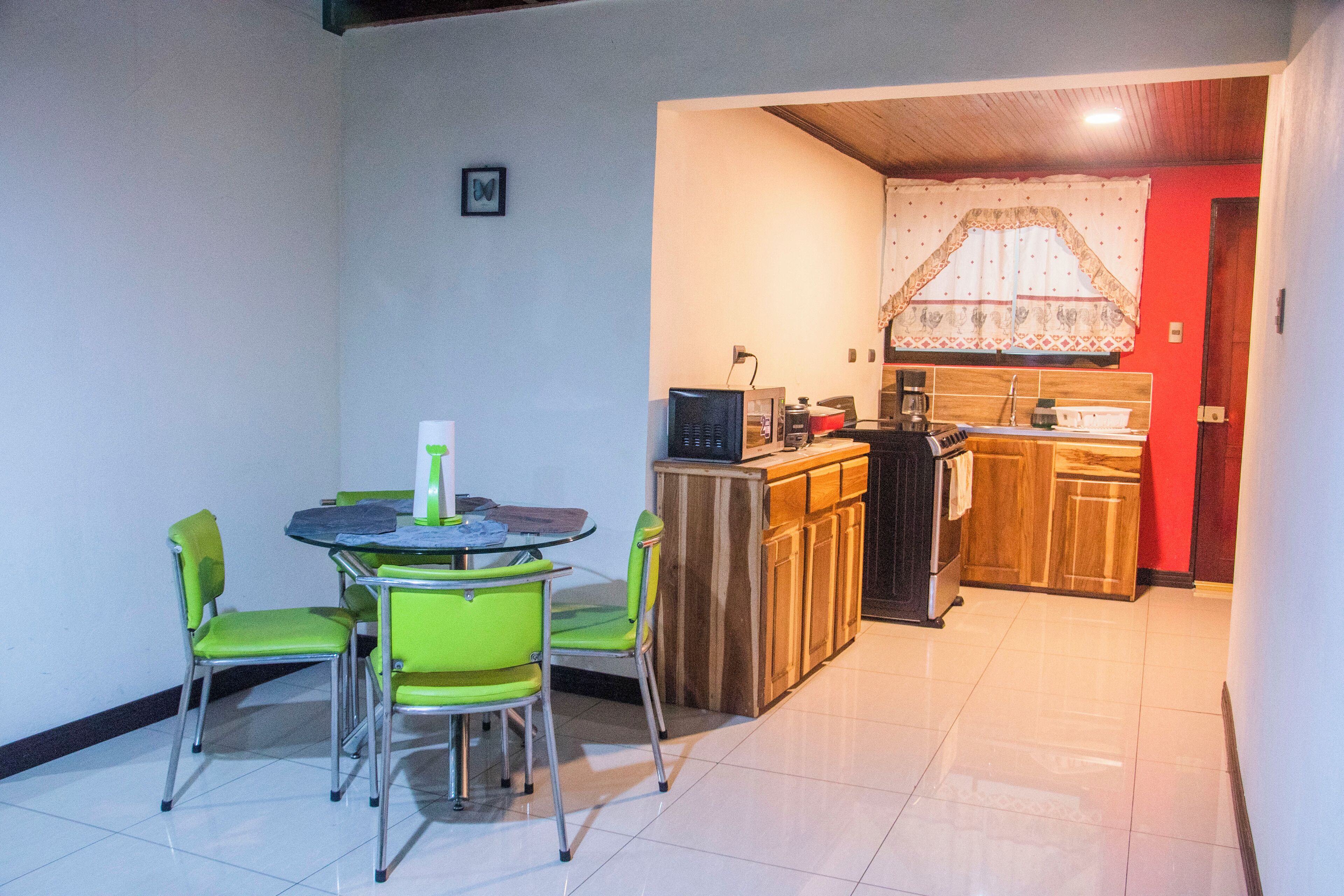 Una cocina compacta con armarios de madera, una mesa de comedor con sillas verdes y un refrigerador pequeño.