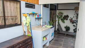 Un baño con lavamanos, un armario de madera, un trapeador y una estantería con productos de limpieza.