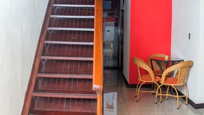 Una escalera de madera conduce a una pared roja, un cristal y sillas de mimbre cerca de una mesa.