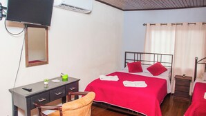 Habitación de hotel con cama, escritorio, silla, espejo y aire acondicionado.
