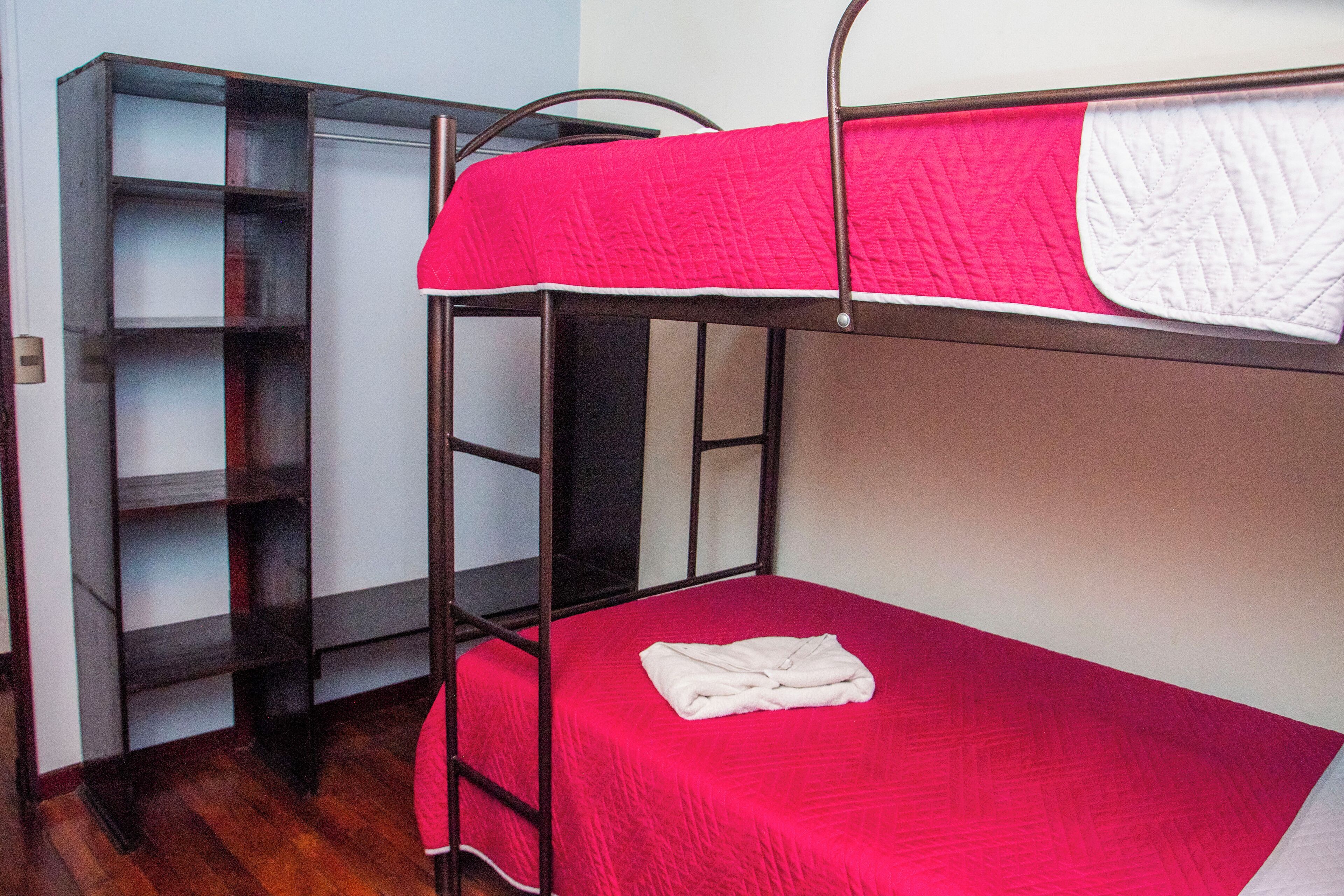 A bunk bed with a red bedspread and a white blanket folded on top. There is a metal ladder attached to the bunk bed.