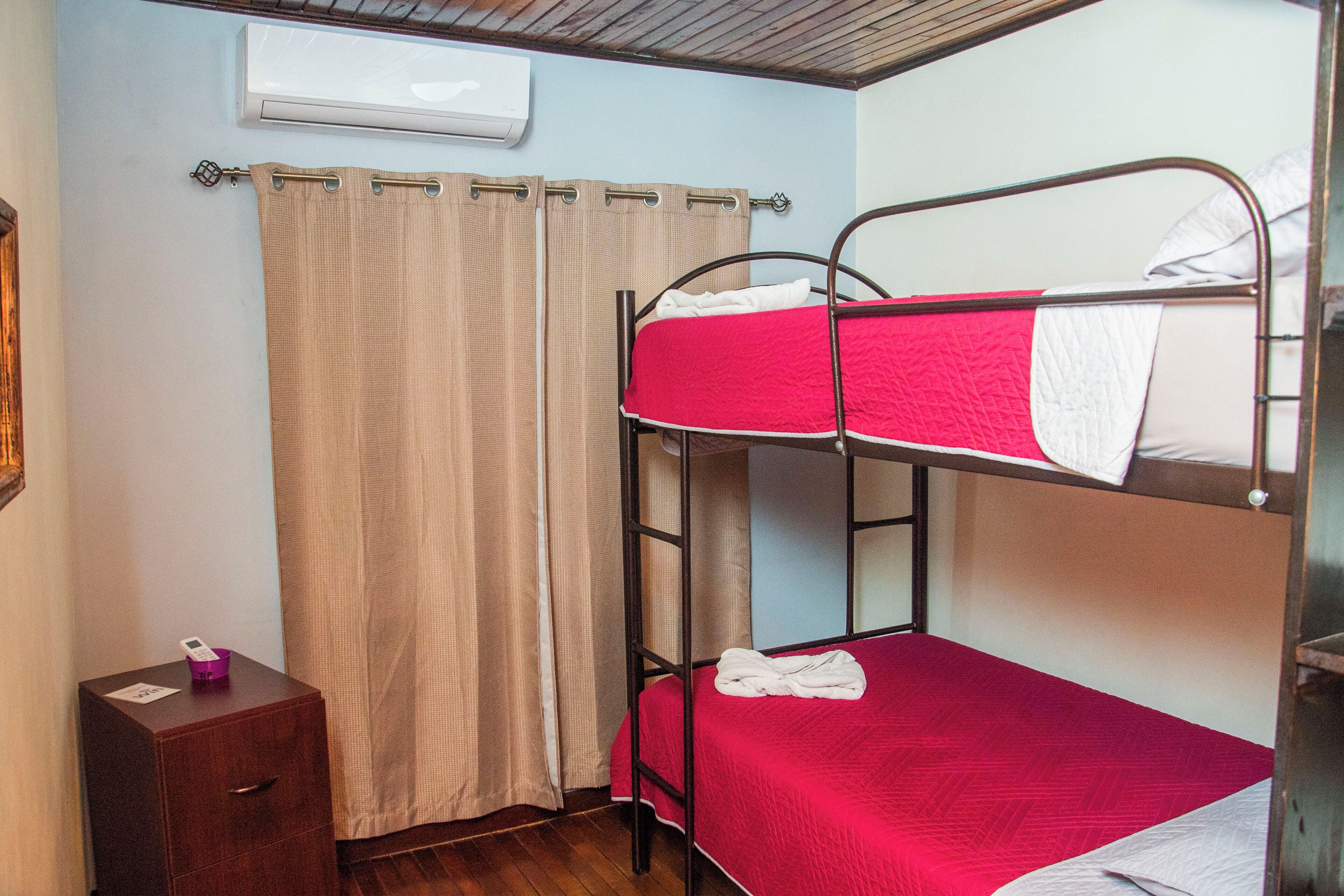 Une chambre avec un lit superposé, un plancher en bois, une petite table de chevet en bois et un rideau.