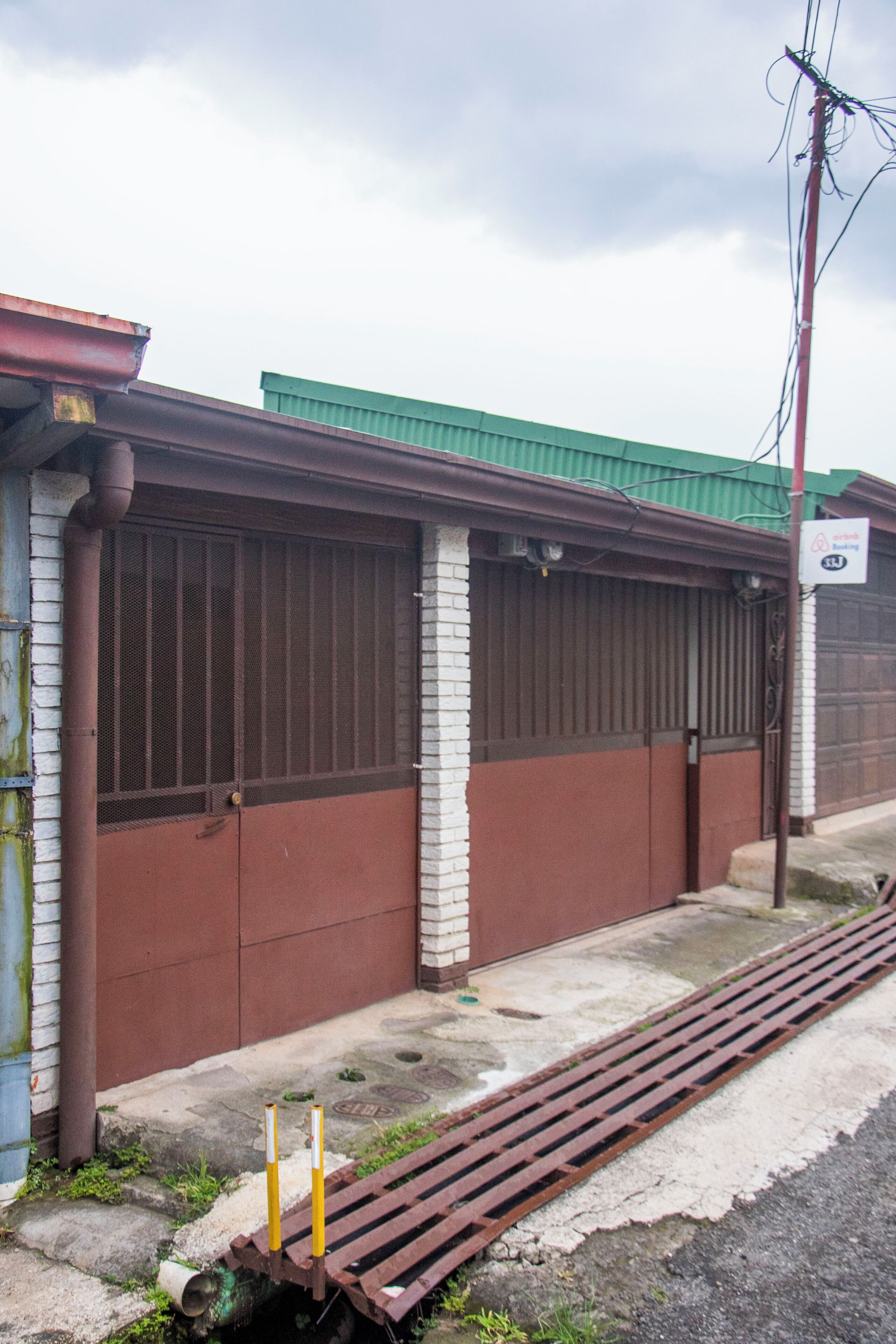 Um edifício com grandes portões de garagem marrons, telhado verde e cerca de metal.