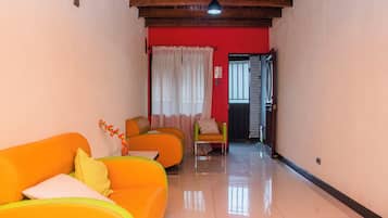 Un pasillo con una pared roja, dos sofás naranjas, un sillón verde y una cortina blanca.