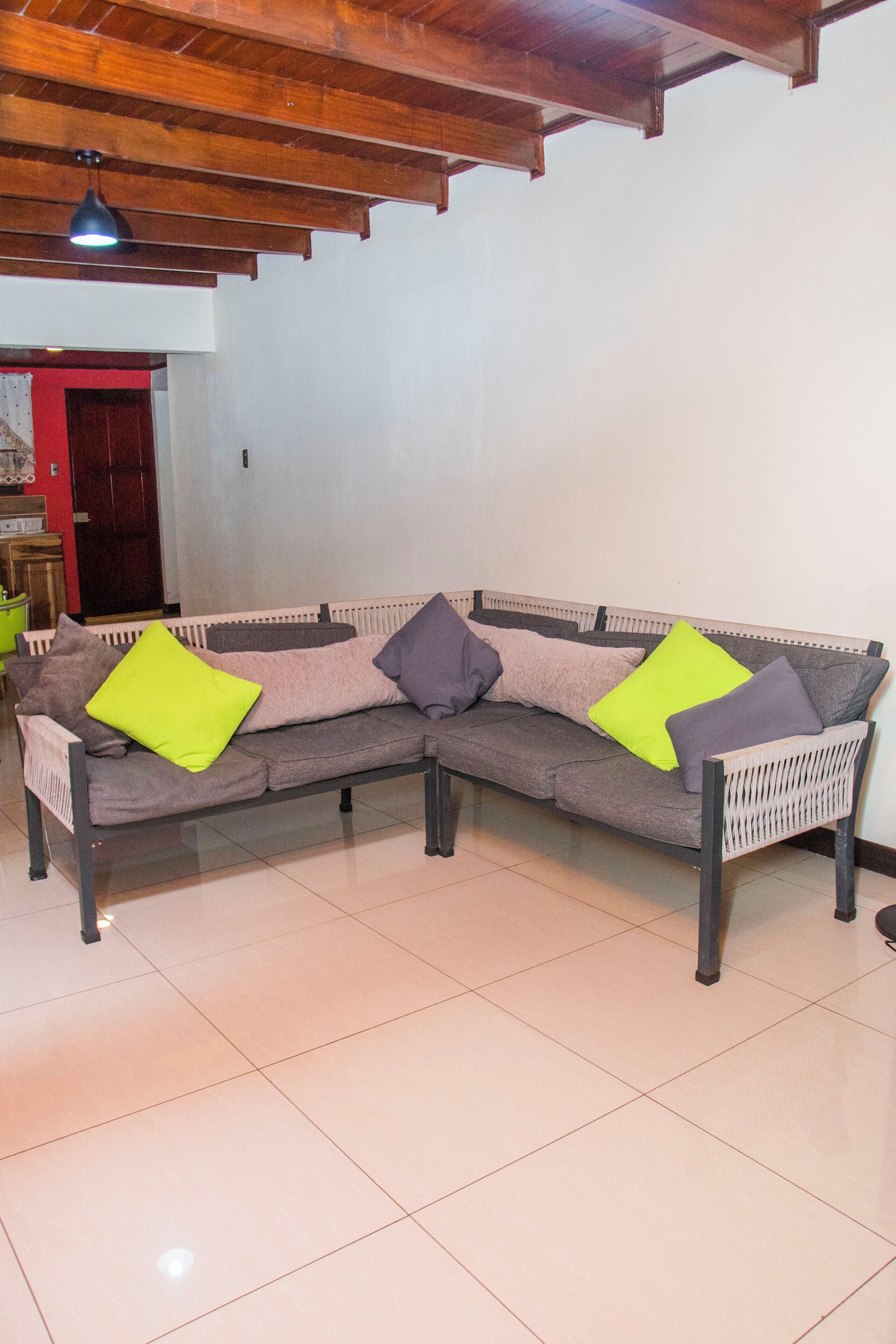 A sectional sofa with multiple cushions in a room with tiled flooring and wooden ceiling beams.