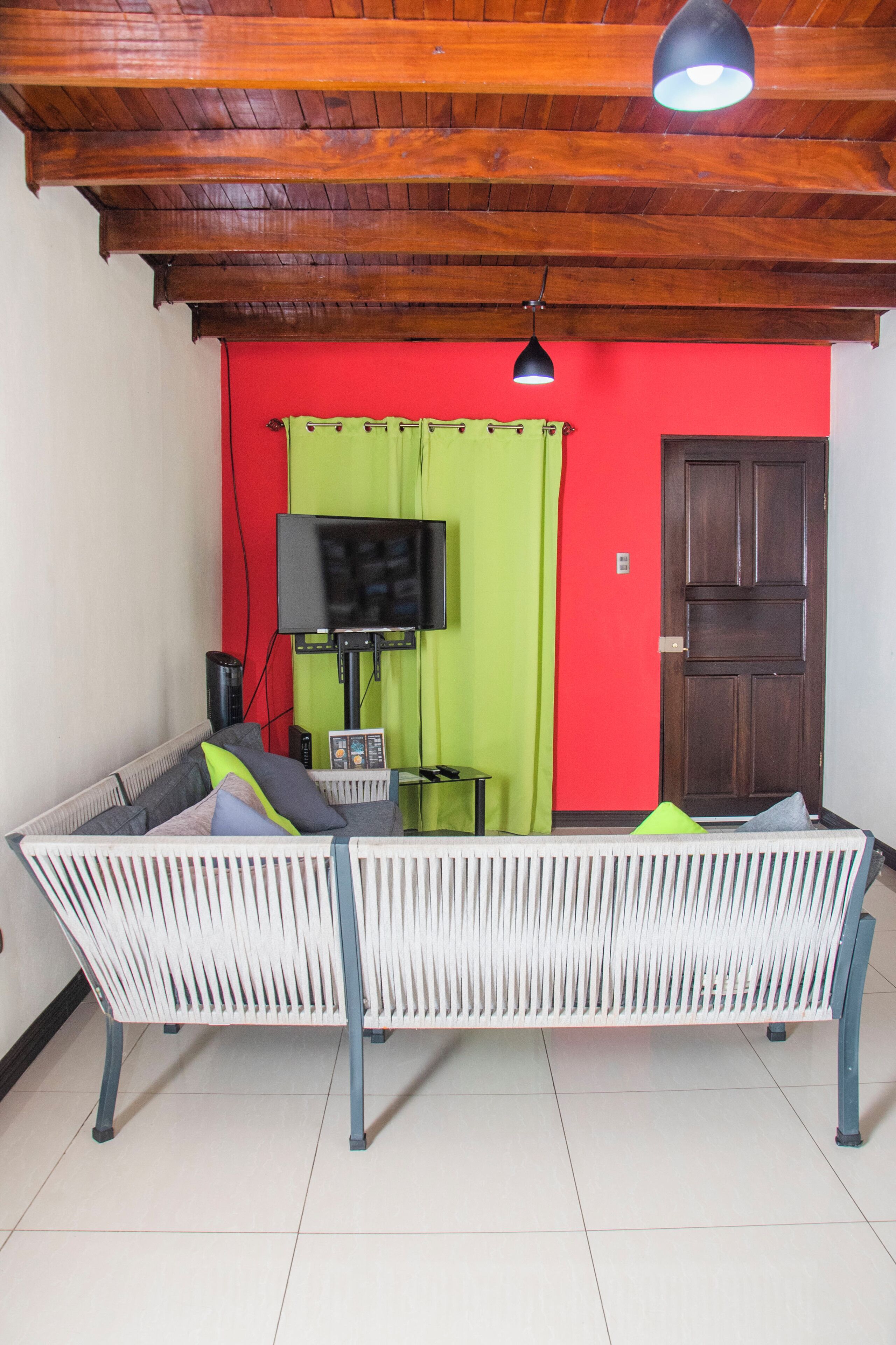 A room with a white sofa, a television on a stand, a green curtain, and a wooden door.