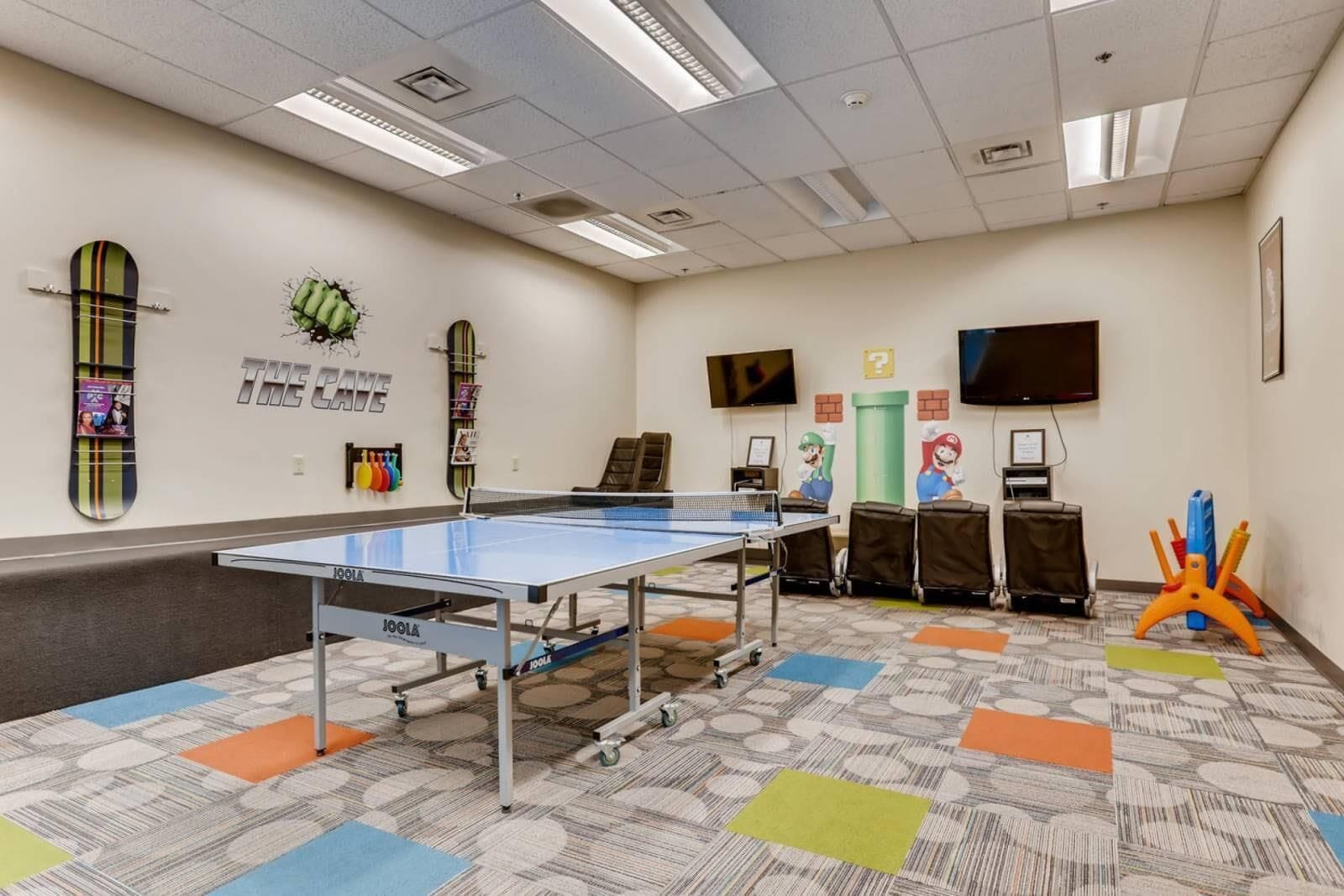 Una habitación con dos mesas de ping pong y dos consolas Nintendo Switch.