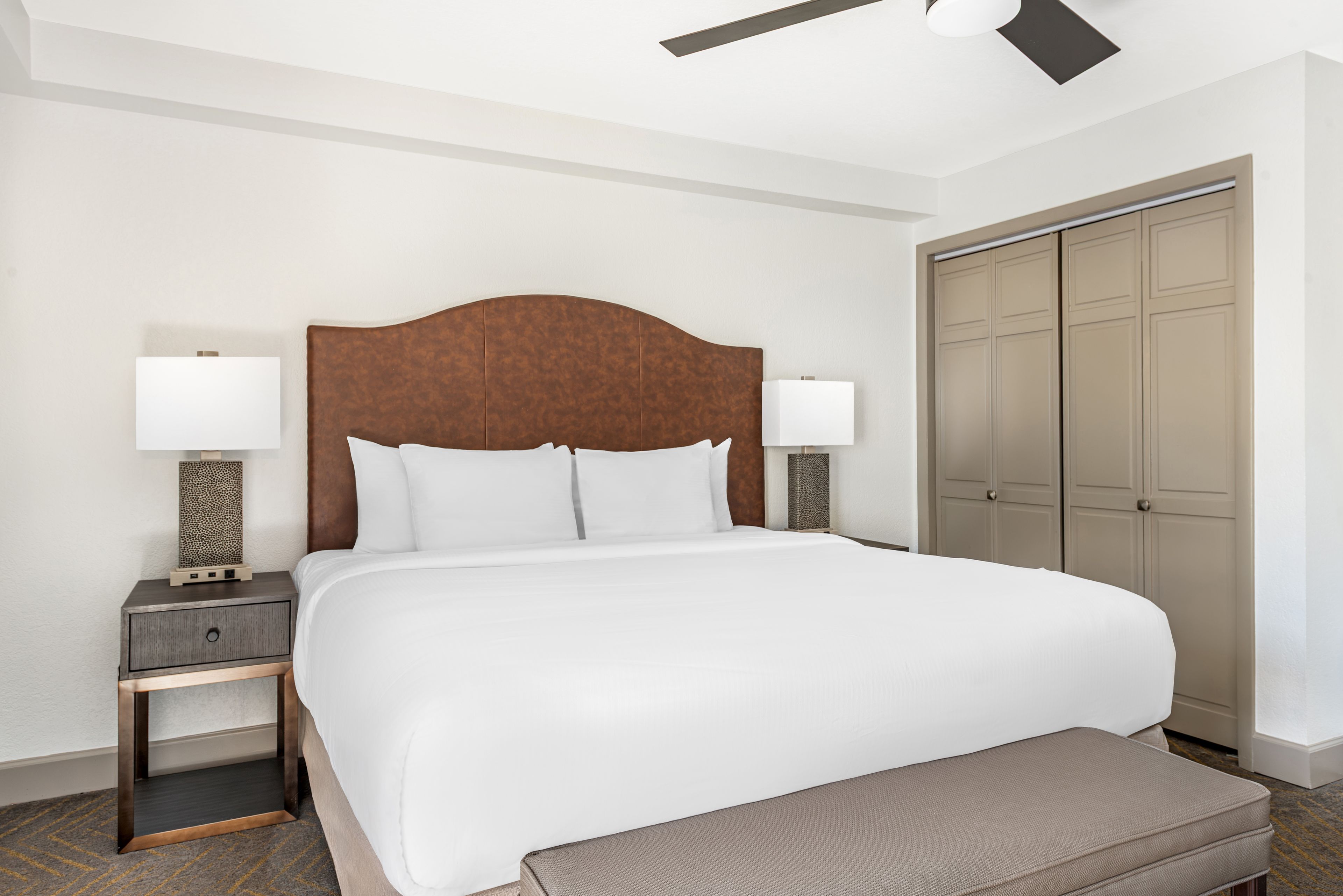 Ein Hotelzimmer mit einem großen Bett, zwei Nachttischen mit Lampen, einem Kleiderschrank und einem Deckenventilator.