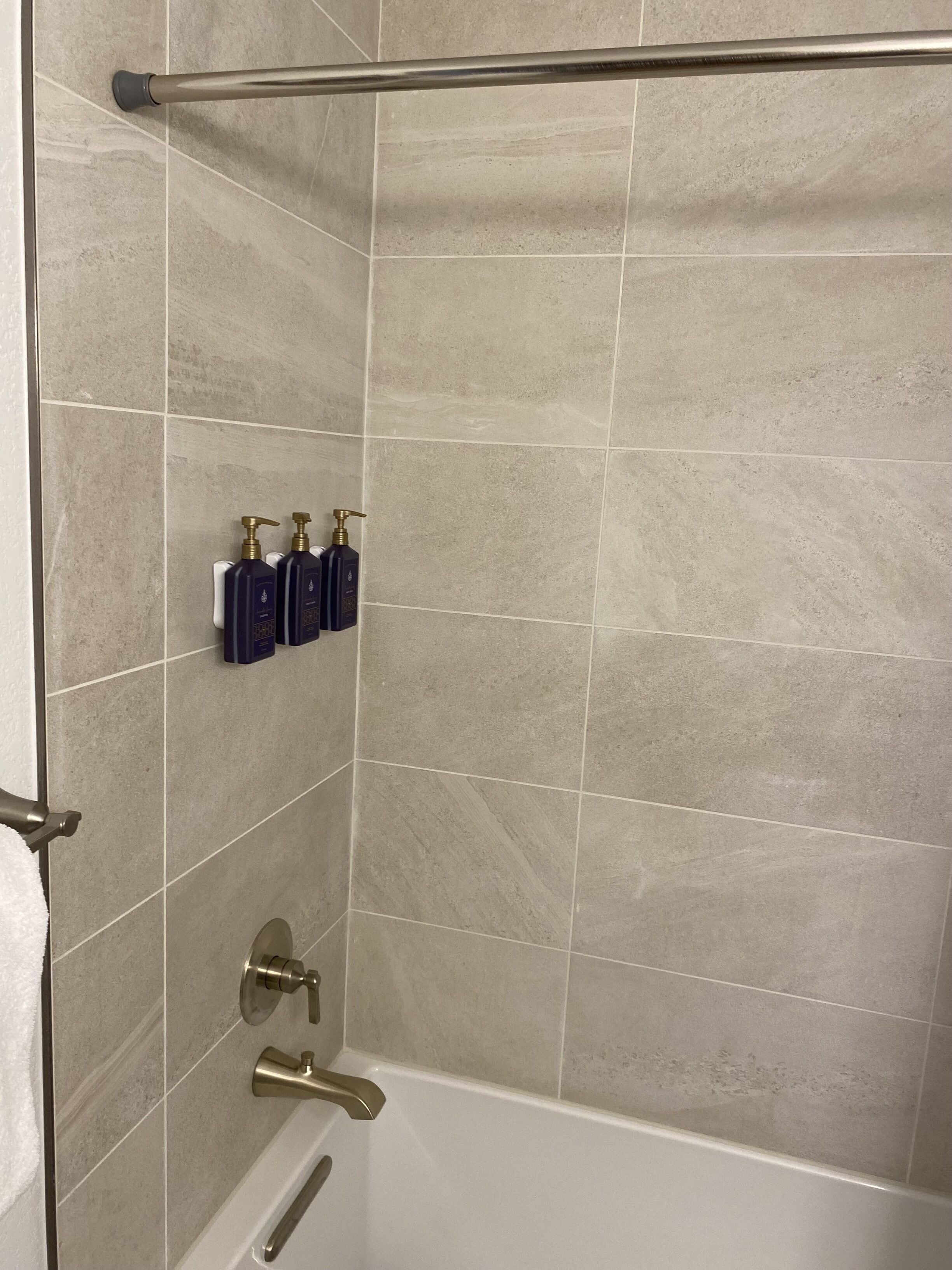 A bathroom with beige tiles, a bathtub, a shower area, and two hand soap dispensers mounted on the wall.