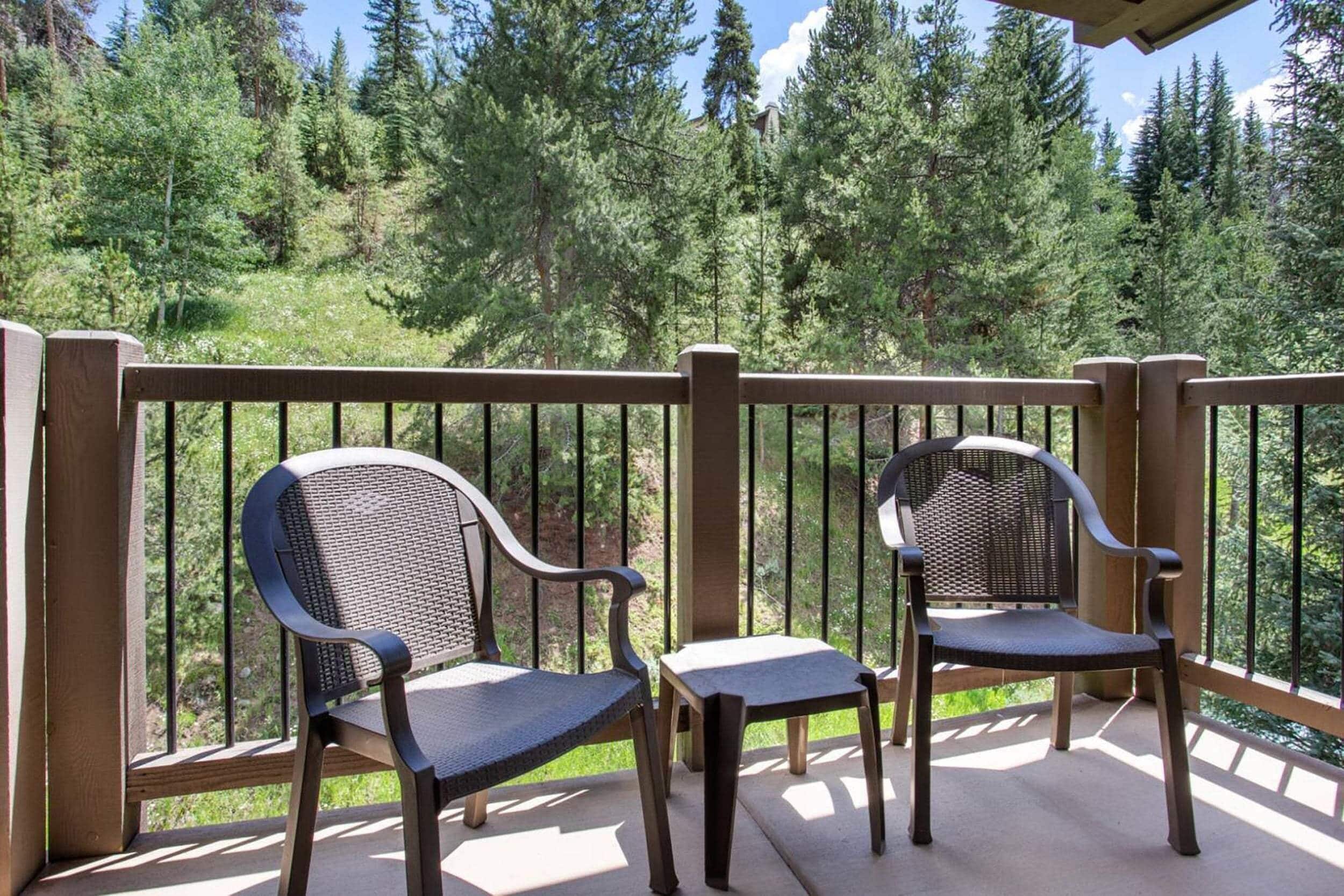 A wooden deck with two chairs and a small table, overlooking a forested area.